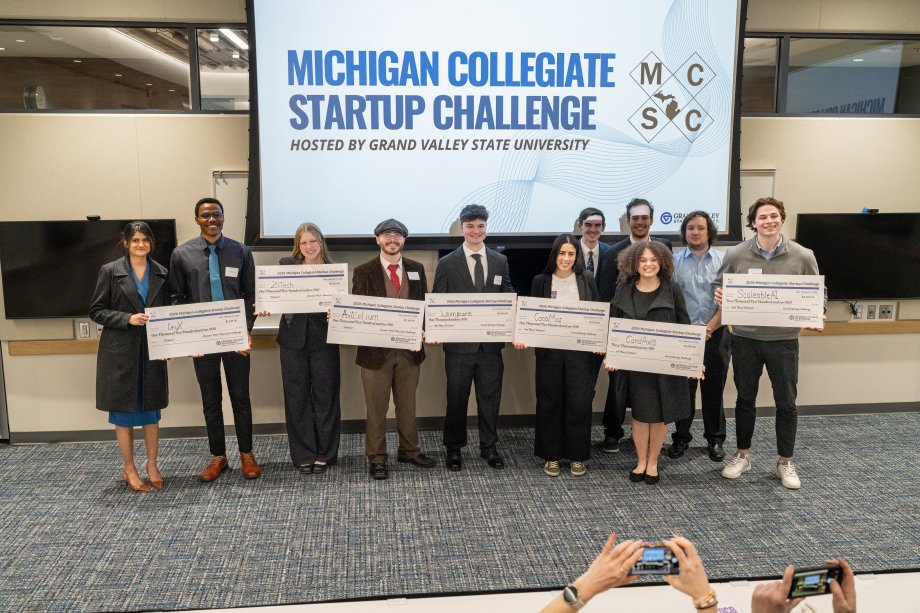 winners of the michigan Collegiate Startup Challenge holding up large checks