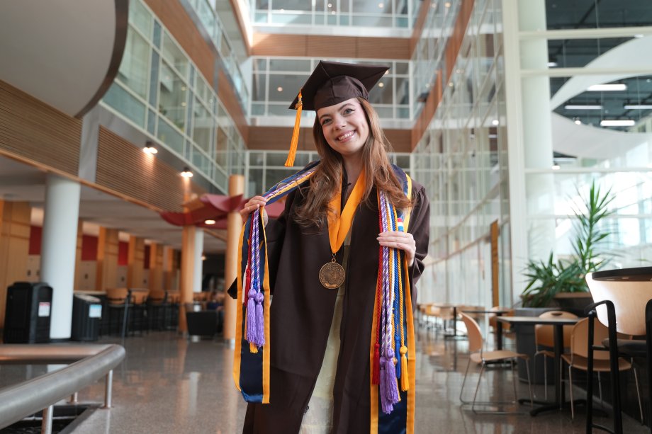 Molly Cochran wears all of her graduation regalia in the College of Health and Human Services atrium.