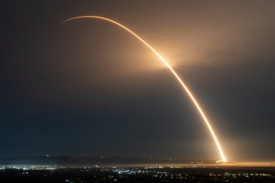 An arc of light cuts through the night sky as a rocket launches into space.