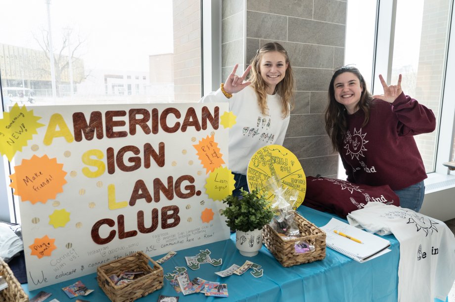 Two students with a sign that says American sign language club.