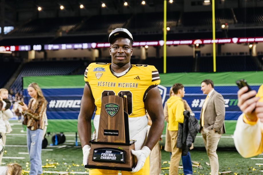 WMU football player smiles while holding the MAC trophy.