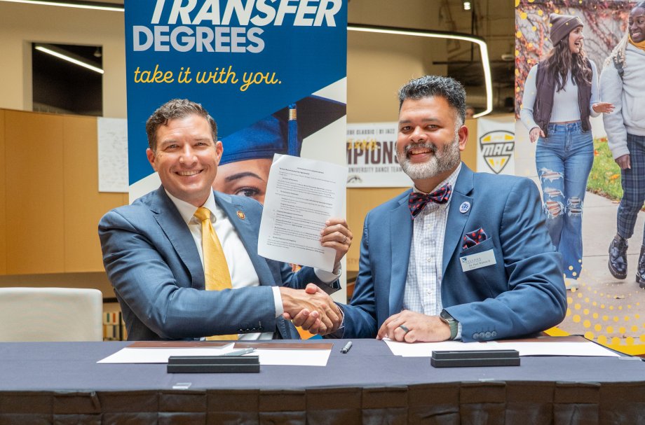 WMU President Russ Kavalhuna and KCC President Paul Watson II shake hands at a table.