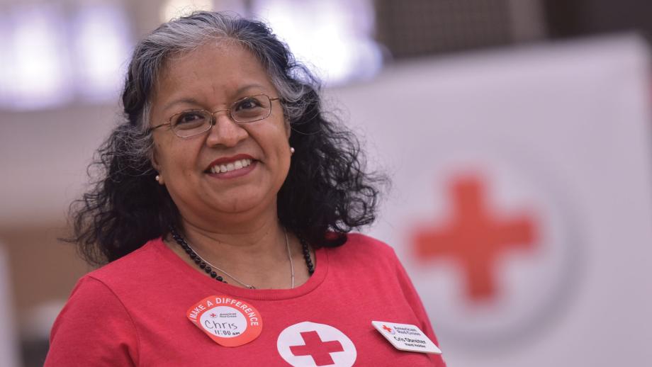 Cris Obretier in front of a soft focus red cross sign in a Red Cross shirt, smiling.