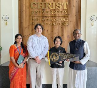 A group of WMU staff pose with partners from Christ University in India. They hold a Western flag.