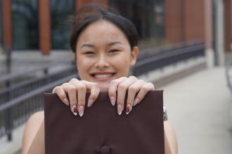 A student holds out her diploma in front of her.