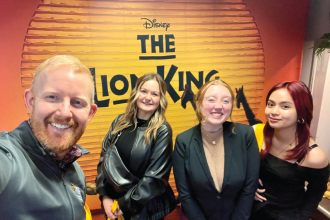 Scott Cowley and three students in front of the Lion King poster