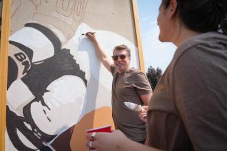 Brad Zenz smiles while painting on a wall.