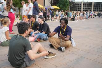 Students sit on the ground during a game at orientation.
