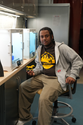 Yoyo Rodriguez-Vargas sits at a 3D printer.