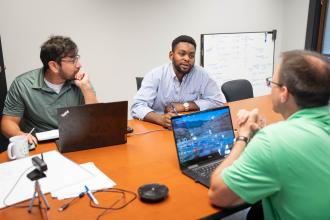 Dan Praise talks with coworkers at a table at Moetion Technologies.