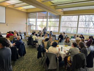 A group of people sitting at round tables chatting before an Evaluation Cafe