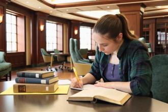Student writing in notebook at table in Reading Room 3014 at Waldo Library.