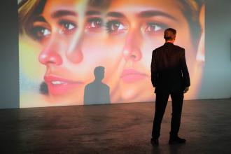 A person stands in front of a large piece of art projected onto a wall.