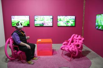 A person sits in a virtual reality headset in a pink room.