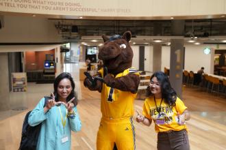 New international students make W hands with Buster Bronco at orientation.
