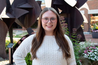 Headshot of Sarah Cook in a white sweater outside of schneider hall