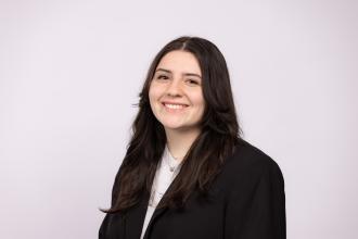 Headshot of Leena Shrum in a black blazer on an off-white background.