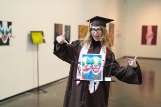 Hope Donovan, dressed in graduation regalia, shows off her painting.
