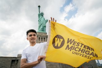 Mehran Najafi holds a Western Michigan University flag in front of the Statue of Liberty.