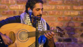 Man sitting and playing an oud, a stringed instrument, in front of a microphone. 