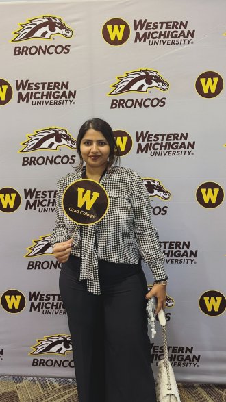 International student from India, Trivedi, stands for photo with WMU wall. 