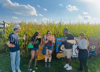 International student from India, Trivedi, stands for photo with WMU students in front of corn field. 