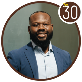 Tae Taylor standing in a suit in front of a green background