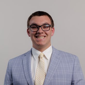 Headshot of Landon Wiedenhoeft in a grey suit with yellow tie on a white background.