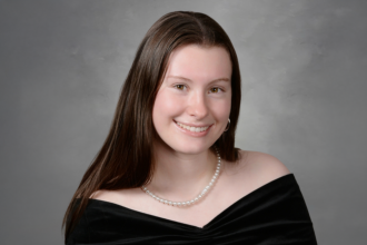 Headshot of Maddie Suttle in a black top on a grey background.