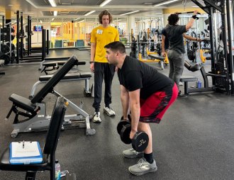 White, male personal trainer working with a white, male participant who is holding 35 pound dumbells and doing a deadlift 