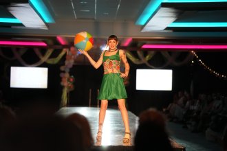Student fashion model holds a beach ball while walking the runway.