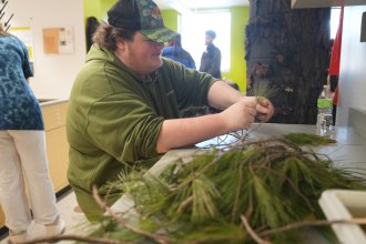 A student arranges evergreen branches on a table.