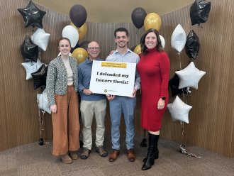 An honors student holds a sign reading "I defended my honors thesis" and is standing with his thesis committee.