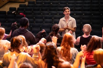 Jack Austin coaches a group of young actors on a stage.