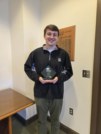 Mason DeRaad holds his Graduate Student Employee Award in the lobby of the Office of Research and Innovation.