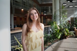 Molly Cochran stands in front of a row of plants in the College of Health and Human Services atrium.