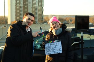 Aidan Ralko and another student hold up a clapperboard while filming his movie.