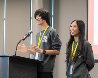 Thien Lohavichan and Gabbi Salud speak to an audience at a podium inside the WMU Student Center.