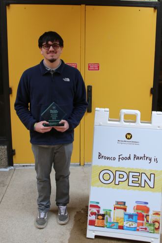 Mario Antonio Valenzuela holds his Undergraduate Student Employee Award in front of the Montgomery Essential Needs Bronco Food Pantry.