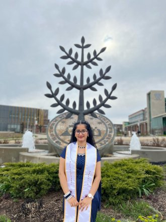An international student poses on campus during graduation season.