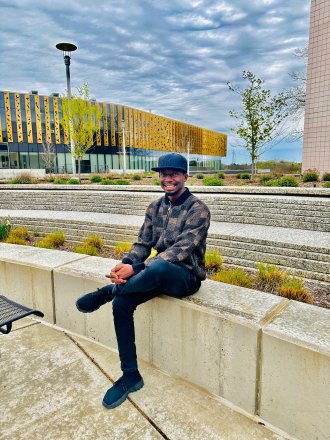 An international student poses on campus in front of the Student Center.