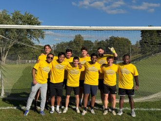An international student poses with his soccer team on the field near the goal.
