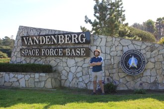 Tom Scott stands in front of the stone sign for Vandenberg Space Force Base.