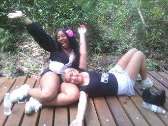 Two WMU study abroad students sit on a deck while raising their arms for a photo.