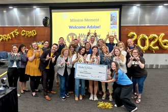 A group of people surrounds Adalae and her mom holding a check from Make-A-Wish.