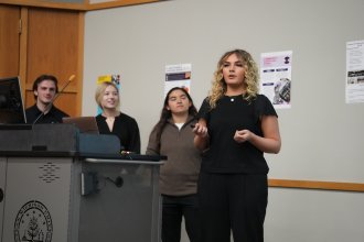 A team of WMU Haworth students presents their consulting project during the spring 2026 capstone gallery walk on campus, with project posters displayed in the background.