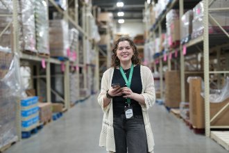 Grace Mulock holds up her cell phone in the aisle of a warehouse.