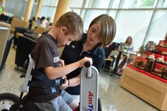Student clinician assisting a child ride a therapy bicycle.