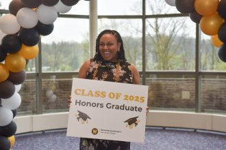 Aniya Thompson at the Spring 2025 honors college graduation ceremony, holding a sign that reads "Class of 2025 Honors Graduate."