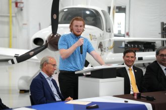 Patrick DeVito talks at a podium in front of an airplane.